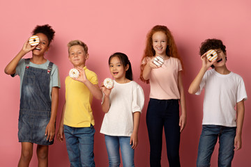 Joyful multiethnic schoolkids with tasty donuts over pink background