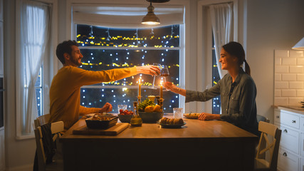 Happy Young Couple in Love Have Romantic Dinner, Toasting Each other with Glasses of Wine, Eating Tasty Meal in the Kitchen, Celebrating, Talking. Beautiful Lovely Husband and Wife Have Romantic Time