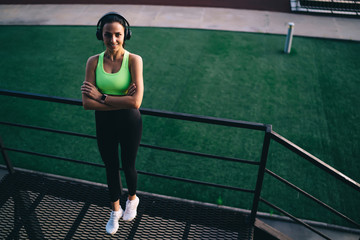 Cheerful sportswoman resting on stairs and listening to music