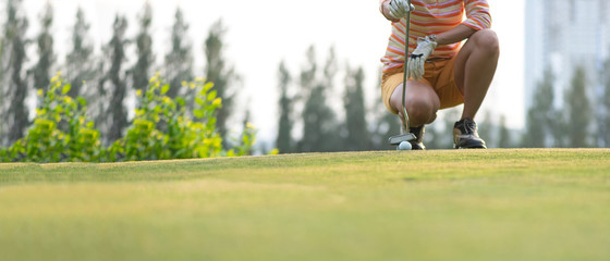 Close up golf ball woman putting golf ball in hole tee with club in golf course on evening on time for healthy sport.   Lifestyle and Sport Concept. copy space and banner