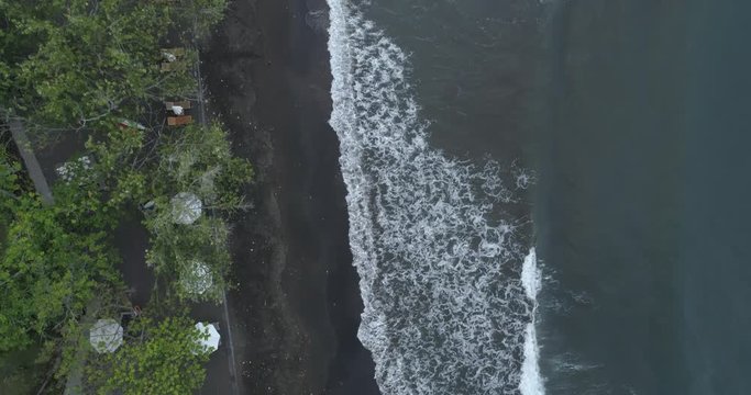 Drone flight over a black sand beach in Bali at sunset