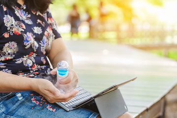 Woman using alcohol nano mist sprayer cleaning her hands to prevent the Coronavirus(Covid-19) and bacterias before use laptop in garden. New normal lifestyle. Health care concept.
