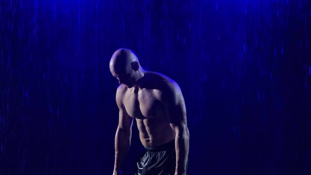 Man performing handstand during crossfit training. A half-naked athletic man is training in the studio among the raindrops and neon blue light. Slow motion. Close up.