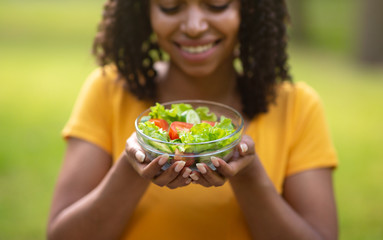 Healthy eating. Happy black girl holding bowl of fresh vegetable salad outdoors, selective focus