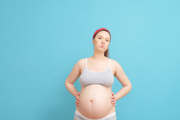 young pregnant woman on blue background, backache