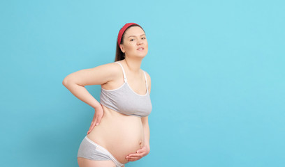 young pregnant woman on blue background, backache