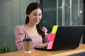 Happy Asian business woman in casual working with laptop and smile looking at camera at modern office or Co-Working Space,Business Startup Concept
