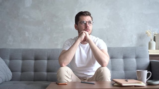 Pensive Young man Sitting on Sofa and Thinking at Home
