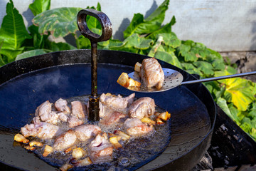 Pieces of bacon and meat are fried in a black pan