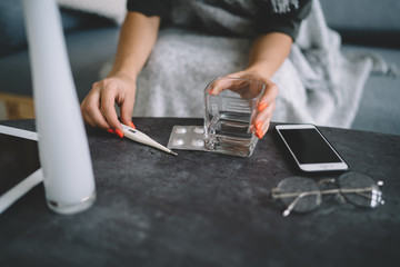 Cropped image of female holding glass with water taking pills from respiratory virus disease care about health, woman talking thermometer for checking temperature suffer from influenza stay at home