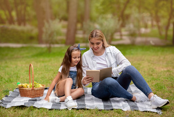 Little Girl Reading Book With Mom On Picnic In Park