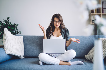 Stressed caucasian woman in eyewear for vision correction checking banking account on laptop computer confused with errors, emotional hipster girl freelancer having trouble with internet connection