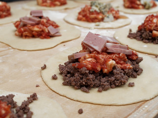 Preparations for a panzerotto, a specialty of southern Italian cuisine. Minced meat, mozzarella and tomato poured as a filling on the dough.