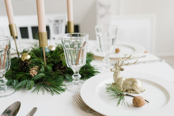 Christmas or new year table setting. Plates, silver Cutlery, glasses, gift box, festive branch decoration, candles, shiny deer on a white table background, selective focus