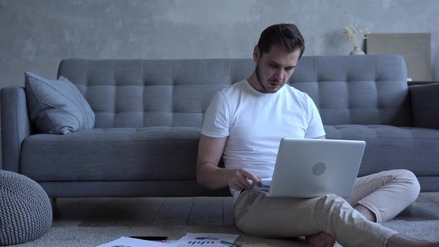 Focused serious man freelancer sitting on floor in cozy living room using computer. Remote job, make review, learn new application concept