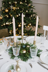 Beautiful glass glasses, candles in the decor of the festive table. Christmas table setting on the background of a Christmas tree