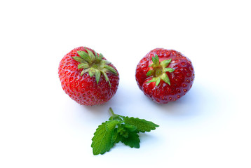 Two ripe strawberries and mint lie on a white background