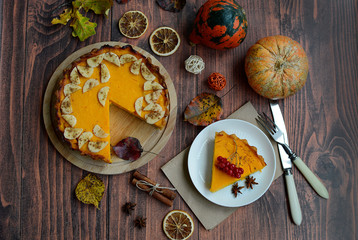 Close-up autumn pumpkin pie, cinnamon sticks, colorful foliage, decorative pumpkins on a dark wooden background