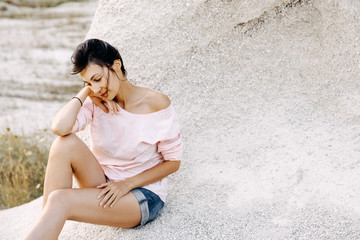 Fototapeta na wymiar Young woman sitting by a cliff on a beach, calm mood.