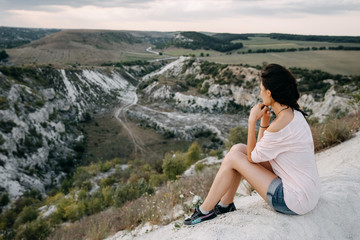Fototapeta na wymiar Young woman sitting on a top of a mountain, looking to a white stone canyon.