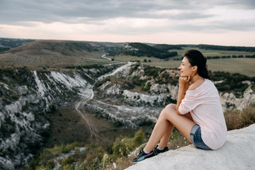Naklejka na ściany i meble Young woman sitting on a top of a mountain enjoying landscapes.