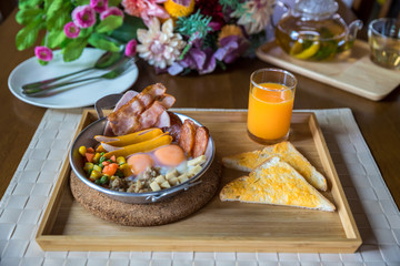 English breakfast in pan with fried eggs, sausages. Panned eggs breakfast set in Thai style street food served on wooden tray with a cup of orange juice and Caesar salad on wood table