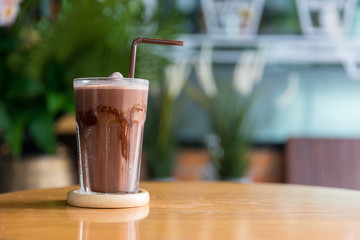 A glass of iced chocolate on table. A glass of Iced Cocoa cool drink served on table. Iced cocoa drink on a wooden table at a cafe. 