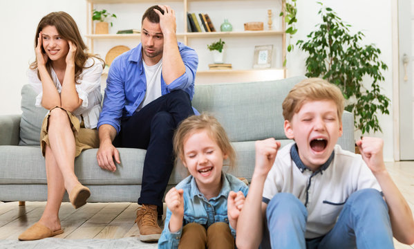 Parents Sitting Exhausted While Children Shouting And Crying At Home