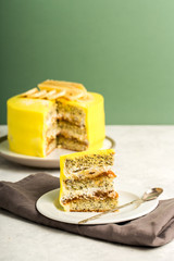 Layered piece of cake with poppy seeds and yellow cream on a white plate for a holiday, light green background, vertical format.