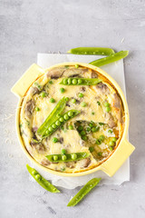 Frittata with, green peas, cheese and champignons in yellow form for baking on light grey background. Vertical format.