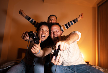 Parents with the children sitting at home on a pleasant evening and playing games on console. They challenge each other to win.		