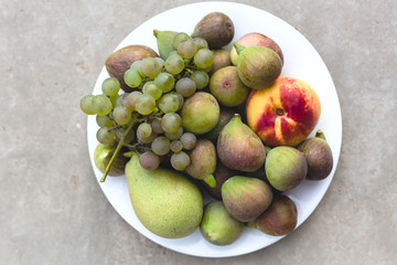 Composition with ripe fresh figs, grape,pear and nectarines on white plate on grey background. Healthy sweet dessert, no calories. Close up, top view,copy space for your text