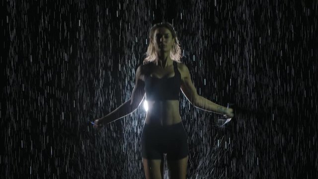 Crossfit rope workout. Sports girl trains in the studio under the streams of rain. Cardio training. Slow motion. Close up.