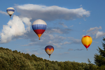 Obraz premium Four multi-colored hot air balloons flying over the summer forest. Some clouds in the sky.
