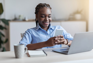 Black female employee using mobile phone at workplace in office, having break