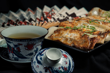 Material of traditional chinese fried dumplings(also called gyoza,pot sticker) on table with black background and decorate with chinese style fans and tea cup.