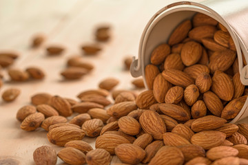 Closeup of brown fresh almonds seed in old aluminium bucket on wooden table.