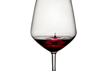 Close-up of a drop of red wine falling into the glass on a white background. Waves are formed in the red wine