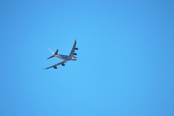 Airplane flying in the clear blue sky, bottom view. Commercial four-engine plane during turn