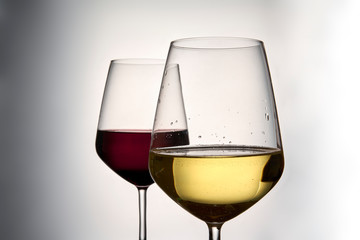 Foreground of two glasses of wine, the first is a glass of white wine, the second is a glass of red wine on a light background
