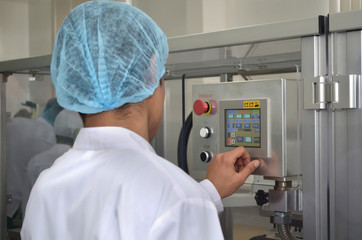 Pharmaceutical industry an employee in a dressing gown and headdress stands at the control panel of an automated production line and manages production