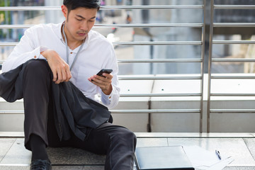 Young businessman who depresss after unemployed . He sit on the floor after fired .  A man sit on the floor in the city. He watch at the id card.