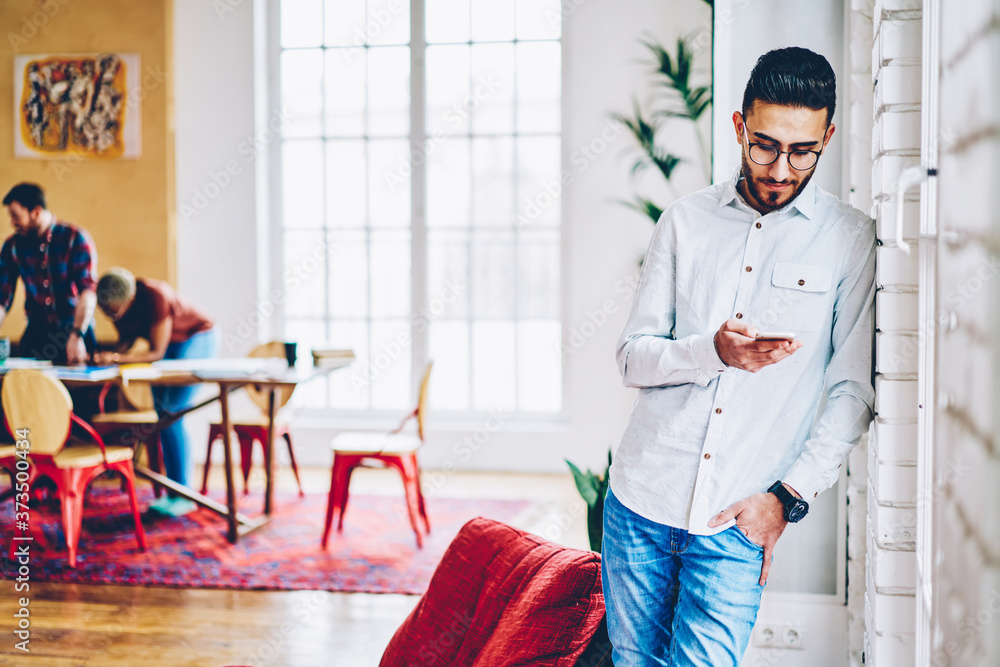 Poster millennial hipster guy in optical eyewear using cellular application for typing content ideas and sh