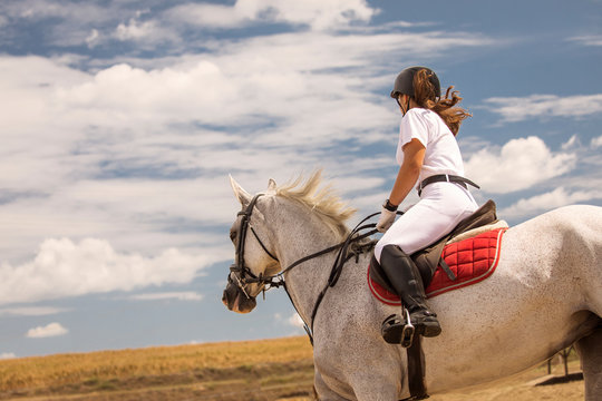 Woman enjoyng hores riding. on a white horse during a beautiful day with white clouds annd blue sky in background, full of joy
