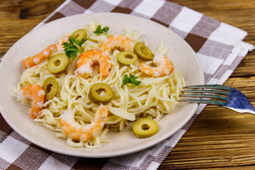 Spaghetti pasta with prawns, green olives and parsley on wooden table
