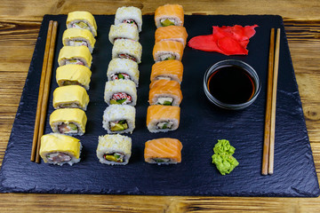 Set of sushi rolls on a black stone slate on wooden table