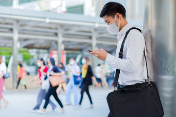 Businessman who put a mask and wear white shirt leaning on the pole in the city while use smartphone. concept business man. 