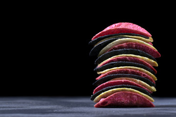 Multicolored potato chips in a stack against the dark background. Copy space