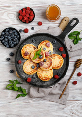 Cottage cheese pancakes with raspberry and blueberry in pan on rustic background, breakfast or lunch