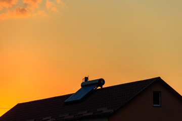 Fototapeta na wymiar Solar water heater on a residential house rooftop at sunset. Renewable energy for house